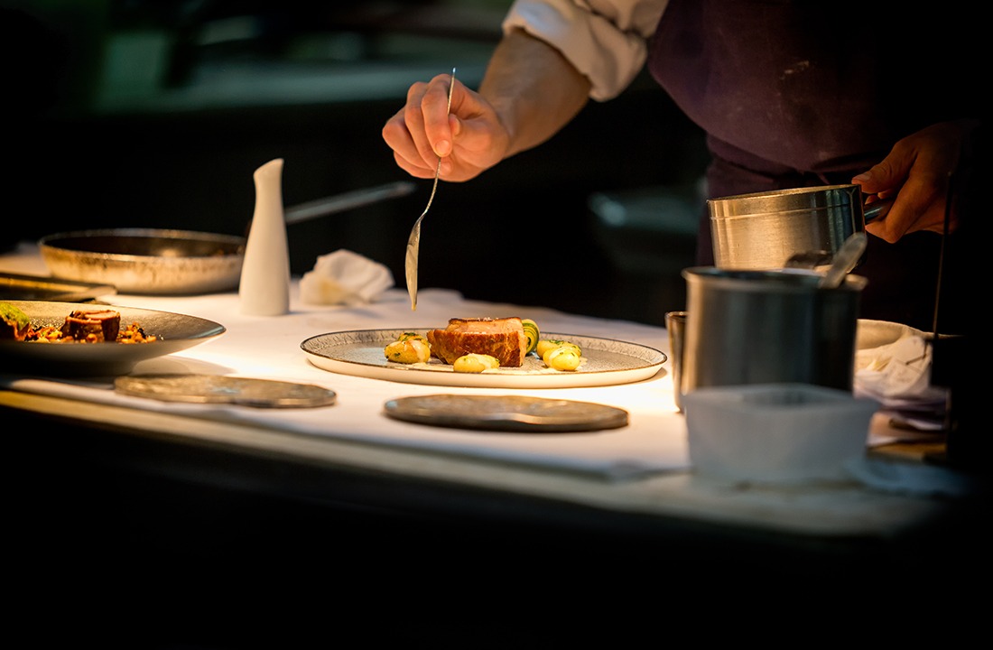 Chef preparing a dish with meat on a plate under a light. The ch