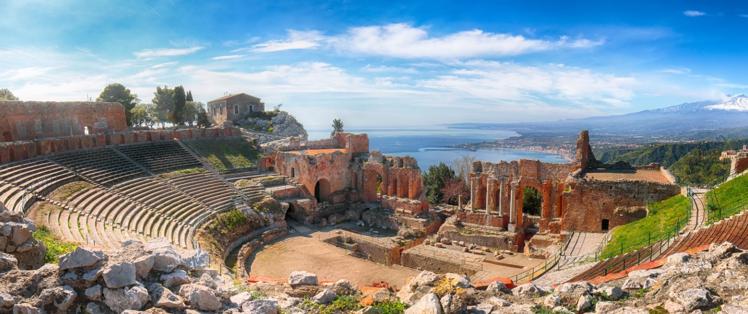 Ruins of ancient Greek theater in Taormina and Etna volcano in the background.